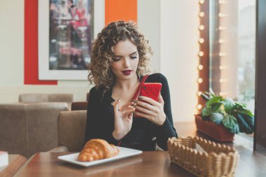 Kafede akıllı telefon kullanan şık bir genç kadın.