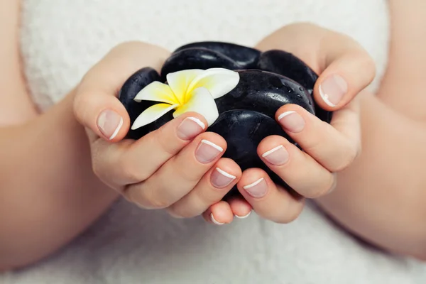 Spa Kobieta Ręce Czarnymi Kamieniami Masażu Piękny Kwiat Tropikalny — Zdjęcie stockowe