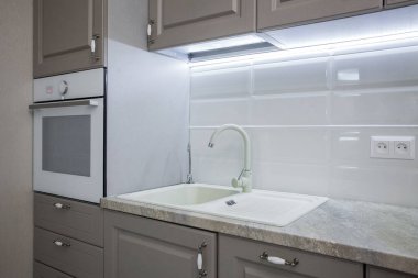 Beyaz lavabosu, musluğu, mermer tezgahı ve rahat dolapları olan mutfak.