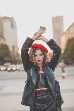 Siyah ceketli ve kırmızı bereli şık bir kadın sokakta poz veriyor. 