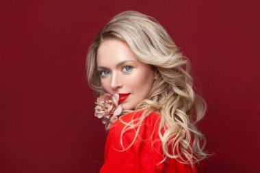 Kırmızı dudaklı güzel bir kadın yüzü. Kırmızı arka planda gülümseyen sarışın kadın model.