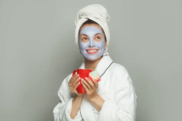 化粧品フェイスマスク中の陽気な楽観的な優しい女性はカップケーキを食べ コーヒーを飲む 女性の日のルーチン — ストック写真