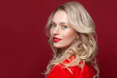 Kırmızı arka planda gülümseyen kadın model. Makyajlı ve kıvırcık saçlı güzel bir kadın.