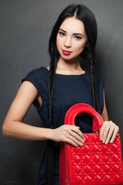 Gri arkaplanda kırmızı el çantası taşıyan zarif, mavi elbiseli genç bir kadının moda fotoğrafı.