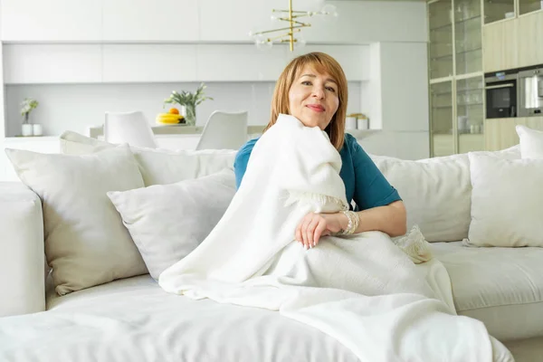 美しい成熟した女性は カメラに笑みを浮かべて 自宅でリラックス暖かい毛布に包まれた快適な座って — ストック写真