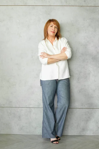 灰色の背景に立って両腕を持つ成熟したビジネス女性 — ストック写真