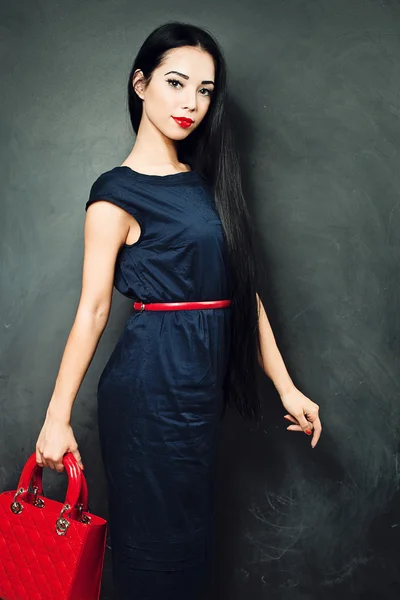 Брюнетка в синем платье и с красной сумкой в руках — стоковое фото
