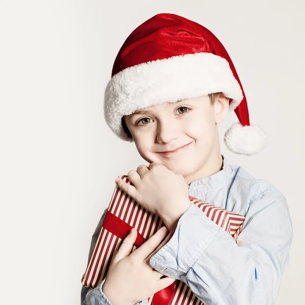 Christmas Kid with Xmas Gift Box. Child Boy with Red Santa Hat a — Stockfoto