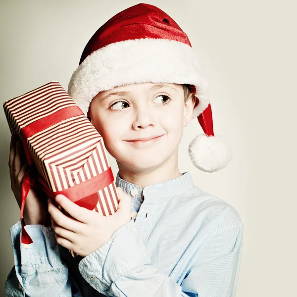 Christmas Child holdind Gift. Happy Little Boy with Santa Hat an — Stok fotoğraf