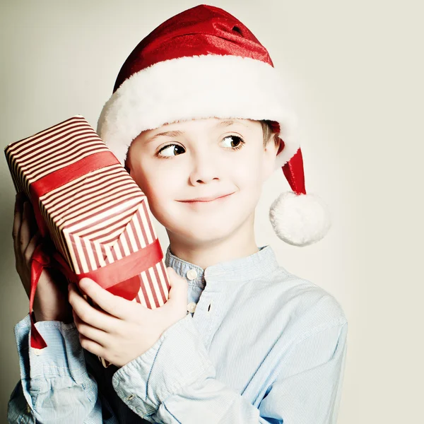 Weihnachtskind mit Weihnachtsmütze. glücklicher kleiner Junge mit Weihnachtsschachtel — Stockfoto