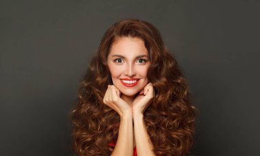 Smiling fashion model woman with shiny skin, wavy hairstyle and red lips makeup on black background 