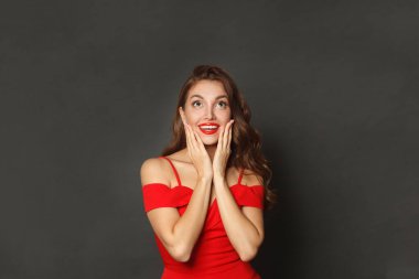 Kıvırcık saç stili ve makyajlı, yüzü siyah arka planda olan sevimli, şaşkın bir kadın.