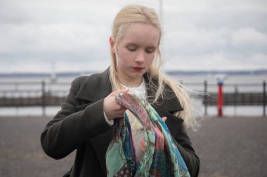 Başörtüsü açık havada duran ciddi sarışın bir kadın.