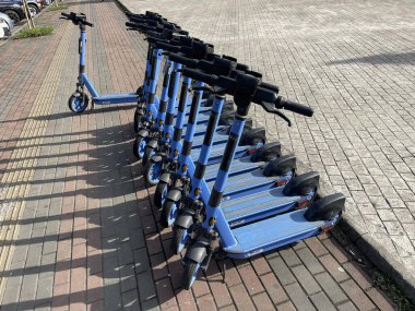 Güneşli bir günde kaldırımda bir sıra scooter kiralanır.