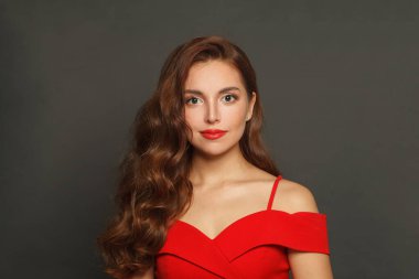 Parlak ciltli, dalgalı saç stili ve siyah arka planda kırmızı dudak makyajı olan model bir kadının kapalı portresi.