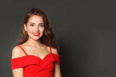 Güzel esmer, şık makyajlı, kahverengi kıvırcık saçlı, siyah arka planda kırmızı dudaklı bir kadın.