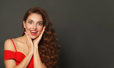 Kıvırcık saç stili ve makyajlı, yüzü siyah arka planda olan, gülen bir kadın.