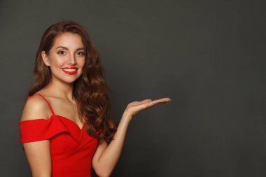 Mutlu model kadın boş avuç içini tutuyor ve siyah arka plandaki kameraya bakıyor.