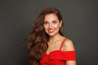 Güzel esmer kadın, modaya uygun makyajlı, kahverengi kıvırcık saçlı, dalgalı saçlı ve siyah arka planda kırmızı dudaklı.