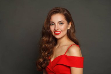 Başarılı esmer, modaya uygun makyajlı, kahverengi kıvırcık saçlı ve siyah arka planda kırmızı dudaklı bir kadın.