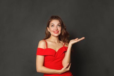 Neşeli model kadın boş avuç içini tutuyor ve siyah arka plana bakıyor.