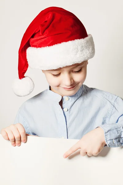 Bambino che indossa il cappello di Babbo Natale punta il dito contro il banner bianco — Foto Stock