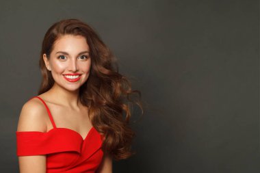 Güzel esmer, modaya uygun makyajlı, kahverengi kıvırcık saçlı, siyah arka planda kırmızı dudaklı bir kadın.