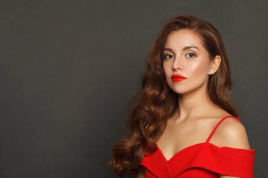 Parlak ciltli, dalgalı saç stili ve siyah arka planda kırmızı dudak makyajı olan model bir kadının moda portresi.