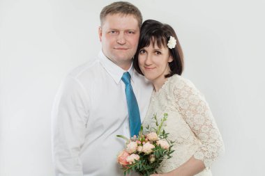 Bir kadın, stüdyoda bir adama arkadan sarılırken elinde buket tutuyor. Hem gülümse hem de mutlu görün. İlkbaharda yapılacak bir kutlama için resmi olarak giyinmişler..