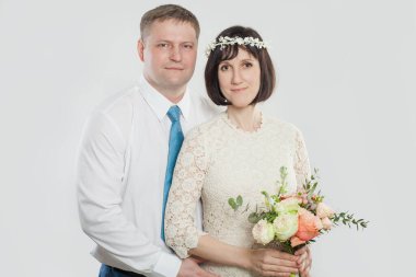 Bir kadın, stüdyoda bir adama arkadan sarılırken elinde buket tutuyor. Hem gülümse hem de mutlu görün. İlkbaharda yapılacak bir kutlama için resmi olarak giyinmişler..