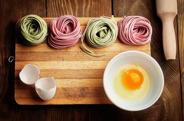 Pasta multicolor, yema de huevo y rodillo daugh sobre mesa de madera — Foto de Stock