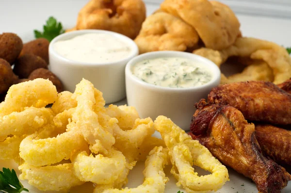 O prato de cerveja com asas de frango picantes, anéis de lula, anéis de cebola fritas, bolas de queijo, pão, molho tártaro e alho — Fotografia de Stock