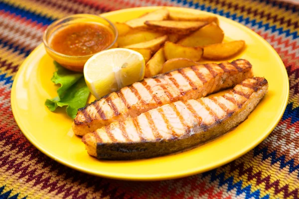 Bife de salmão grelhado com batatas e molho em um prato amarelo — Fotografia de Stock