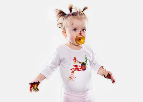 The baby girl with a pacifier in gouache soiled hands and shirt isolated — Stock Photo, Image