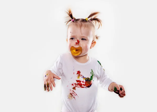 The baby girl with a pacifier in gouache soiled hands and shirt isolated — Stock Photo, Image