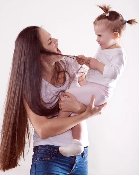 La joven madre con el pelo castaño largo en jeans sosteniendo a un bebé — Foto de Stock