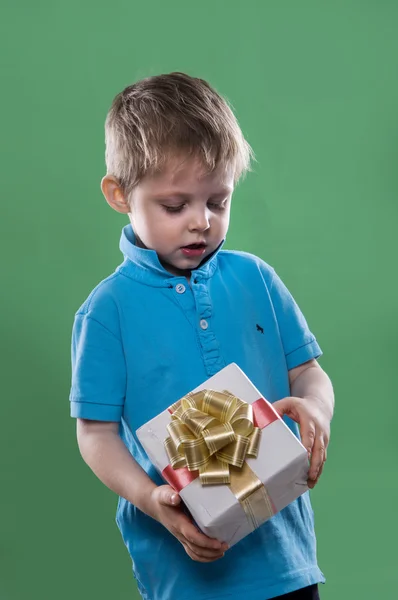 Un petit garçon tenant une boîte cadeau dans ses mains sur le fond vert — Photo