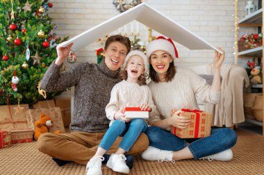 Mutlu Noeller! Güzel bir anne, baba ve kız Noel ağacının yanında çatı sembolü.. 