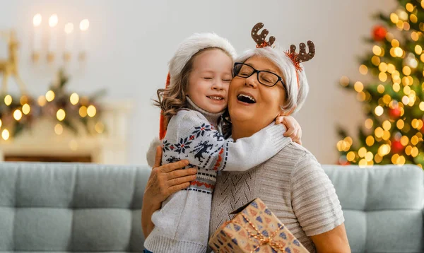 Premium Photo  Merry christmas and happy holidays! cheerful grandma and  her cute grand daughter girl exchanging gifts. granny and little child  having fun near tree indoors. loving family with presents in