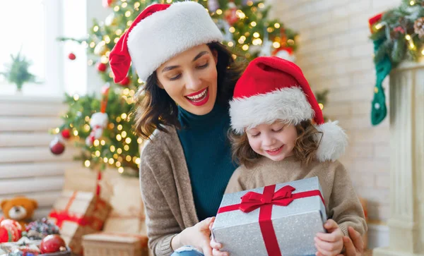 メリークリスマスとハッピーホリデー 陽気な母親とかわいい娘の女の子は贈り物を交換します 屋内で木の近くで遊んでいる親と小さな子供 プレゼント付きの家族を愛する — ストック写真