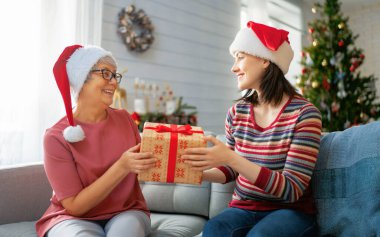 Mutlu Noeller ve mutlu tatiller! Kıdemli anne ve yetişkin kızı hediye değiş tokuşu yapıyor. İçerideki ağacın yanında eğleniyoruz. Odasında hediyeler olan sevgi dolu bir aile. 