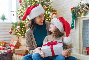 Mutlu Noeller ve mutlu tatiller! Neşeli anne ve tatlı kızı hediye değiş tokuşu yapıyor. Ebeveyn ve küçük çocuk kapalı alanda eğleniyorlar. Odasında hediyeler olan sevgi dolu bir aile.   