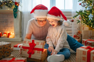 Mutlu Noeller ve mutlu tatiller! Neşeli büyükanne ve tatlı torunu hediye değiş tokuşu yapıyor. Büyükanne ve küçük çocuk içeride ağacın yanında eğleniyorlar. Odasında hediyeler olan sevgi dolu bir aile.