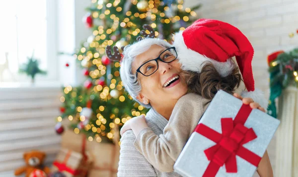 メリークリスマスとハッピーホリデー 陽気な祖母と彼女のかわいい壮大な娘の女の子は贈り物を交換します おばあちゃんと小さな子供が屋内で木の近くで楽しんでいます プレゼント付きの家族を愛する — ストック写真