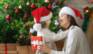 Mutlu Noeller ve mutlu tatiller! Neşeli anne ve tatlı kızı hediye değiş tokuşu yapıyor. Ebeveyn ve küçük çocuk kapalı alanda eğleniyorlar. Odasında hediyeler olan sevgi dolu bir aile.   