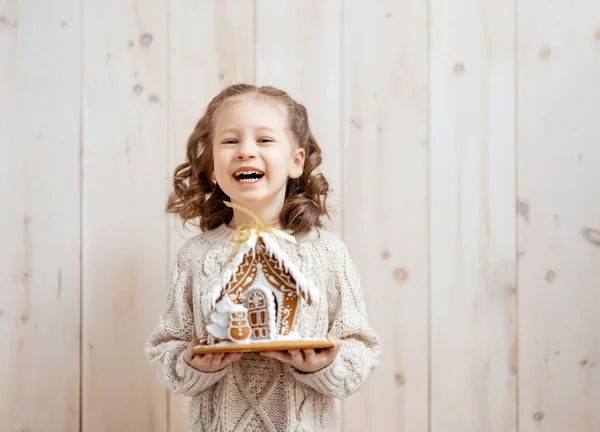 幸せな女の子とともにクリスマスジンジャーブレッドハウス上の白い木の背景 — ストック写真