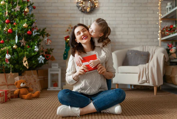 メリークリスマスとハッピーホリデー 陽気な母親とかわいい娘の女の子は贈り物を交換します 屋内で木の近くで遊んでいる親と小さな子供 プレゼント付きの家族を愛する — ストック写真