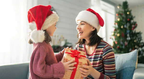 メリークリスマスとハッピーホリデー 陽気な母親とかわいい娘の女の子は贈り物を交換します 屋内で木の近くで遊んでいる親と小さな子供 プレゼント付きの家族を愛する — ストック写真