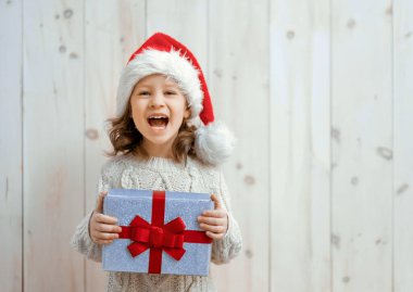 Mutlu küçük kız Noel hediyesi ile beyaz ahşap arka planda. 