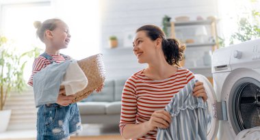 Güzel genç kadın ve kız çocuk küçük yardımcı evde çamaşır yıkarken eğleniyor ve gülümsüyor..